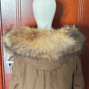 May include: A brown hooded coat with a large fur collar. The fur collar is a mix of brown, tan, and black. The coat is displayed on a mannequin head.