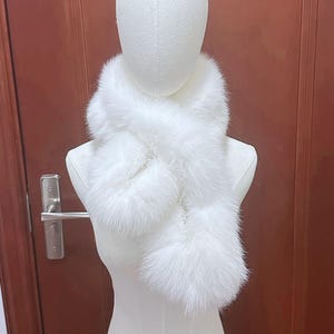 Puede incluir: Bufanda de piel sintética blanca y esponjosa, colocada sobre un maniquí. La bufanda tiene un diseño cruzado y una apariencia suave y lujosa. Un accesorio de invierno.