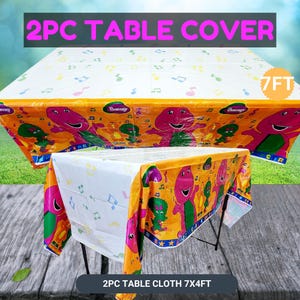 May include: A two-piece table cover set. The table covers feature a colorful design with a purple dinosaur character and musical notes on a white and orange background. The table cloth measures 7 feet by 4 feet.