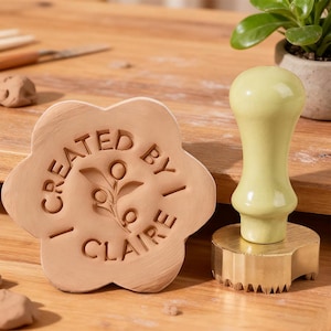 May include: A light brown clay stamp with the text "CREATED BY CLAIRE" and a floral design, alongside a light green and gold clay texture tool. The stamp is flower-shaped.