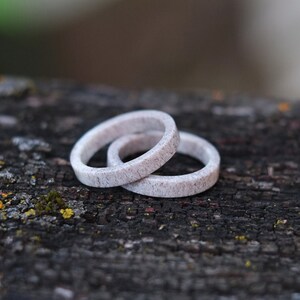 May include: Two white rings made of antler bone, stacked on top of each other, on a dark brown wooden surface with green moss.