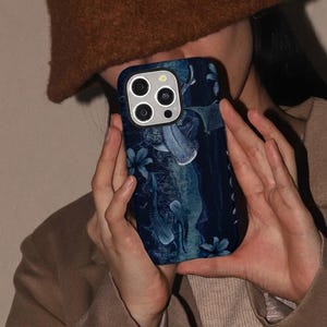 May include: A dark blue phone case featuring a marine design with whale sharks and floral accents. The case has a glossy finish and a camera cutout. The design incorporates shades of blue and white, creating a visually appealing aesthetic.