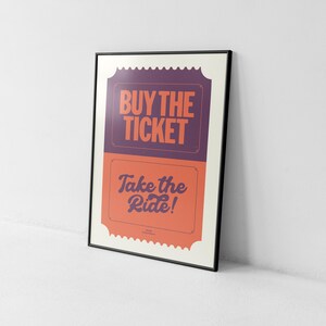May include: Framed poster with the text "BUY THE TICKET" in a purple section and "Take the Ride!" in an orange section. The poster has a black frame and a white border.