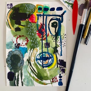 Puede incluir: Una pintura abstracta en acuarela sobre papel blanco con formas superpuestas en verde, azul y rojo con gotas de tinta, junto a un pincel de mango negro, una herramienta de plástico roja y un papel pequeño con muestras de pintura.