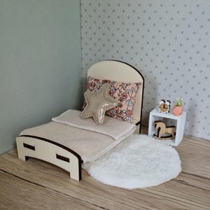 Pode incluir: Conjunto de quarto em miniatura com uma cama de madeira, uma almofada floral e uma almofada em forma de estrela. Uma pequena mesa de cabeceira branca com um relógio, uma planta e um cavalo de baloiço de madeira. Um tapete branco fofo.