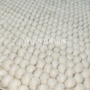 May include: Close-up of a white, textured rug with a repeating pattern of rounded, raised elements. The rug's surface is densely packed with these soft, spherical shapes, creating a tactile and visually interesting design. The brand name "WovynRugs" is visible.