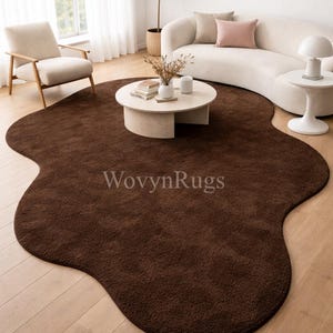 Könnte beinhalten: Ein dunkelbrauner, unregelmäßig geformter Teppich in einem Wohnzimmer. Der Teppich hat eine weiche, plüschige Textur und liegt auf einem hellen Holzboden. Die ungewöhnliche Form des Teppichs verleiht dem Raum ein besonderes Designelement.