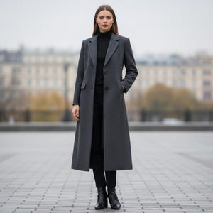May include: A long, charcoal grey coat with a classic design. The coat features a notched lapel, button closures, and pockets. The person in the image is wearing a black turtleneck and black trousers, paired with black ankle boots. The coat is a stylish outerwear option.