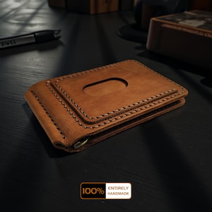 Pode incluir: Uma carteira de couro castanho feita à mão com um clip para dinheiro. A carteira apresenta um design costurado e um recorte para fácil acesso. A imagem inclui o texto "100% ENTIRELY HANDMADE".
