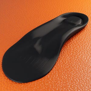 Può includere: Una soletta nera dal design sagomato, appoggiata su una superficie arancione strutturata. La soletta è sagomata per adattarsi al piede, con un tallone rialzato e supporto plantare. La superficie ha una trama granulosa.