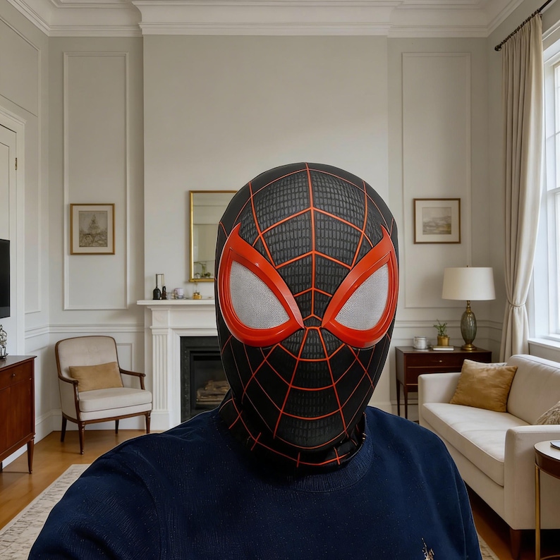 May include: A black and red Spider-Man mask with a web pattern and large eye openings. The mask has red trim around the eyes and a black background. The mask is worn by a person wearing a blue shirt.