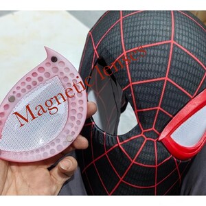 May include: A black and red Spider-Man mask with a web pattern and red eye details. A pink, teardrop-shaped magnetic lens is held next to the mask, with the word "Magnetic" printed on it.