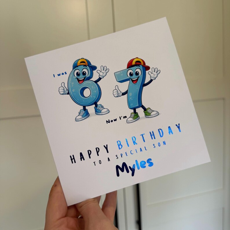 May include: A square white birthday greeting card featuring two cartoon number characters, a six and a seven, wearing baseball caps and sneakers. The text reads: I was 6, Now I'm 7, HAPPY BIRTHDAY TO A SPECIAL SON, and the name Myles in blue.