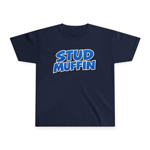 Puede incluir: Camiseta azul marino con la frase "STUD MUFFIN" en una fuente audaz, azul y blanca con contorno. El texto está centrado en la parte delantera de la camiseta. La camiseta está hecha de un material suave.