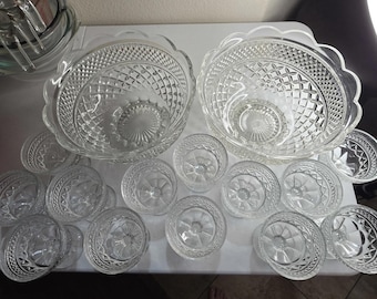 May include: A clear glass punch bowl set featuring two large bowls and twelve smaller matching cups. Each piece displays a pressed diamond pattern on the exterior, a scalloped rim, and a starburst design on the base of the interior.
