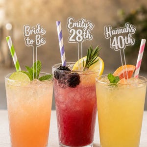 Può includere: Tre miscelatori per bevande in acrilico trasparente con scritte personalizzate Bride to Be, Emily's 28th e Hannah's 40th. Ogni miscelatore è inserito in un bicchiere alto pieno di ghiaccio, bevande alla frutta colorate e cannucce di carta.