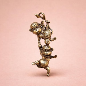 May include: A bronze-colored sculpture of three monkeys. One monkey hangs from a branch, supporting another monkey on its head, while the third monkey stands below, balancing on one leg. The sculpture has a detailed, textured finish.