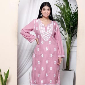 May include: A light pink, long-sleeved kurta and matching pants set. The outfit features intricate white floral embroidery on the neckline, sleeves, and pants. The kurta has a V-neck and the pants are wide-legged.