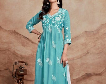 May include: A turquoise tunic with white floral embroidery and three-quarter sleeves. The tunic has a V-neck and a gathered waist. It is paired with white palazzo pants with a lace trim. The outfit is suitable for casual or semi-formal occasions.
