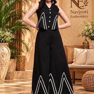 May include: A black sleeveless vest with a V-neckline and white button closures, paired with matching wide-leg trousers. Both pieces feature a prominent white zigzag trim along the hemline. The vest has a pointed front hem and the trousers are floor-length.