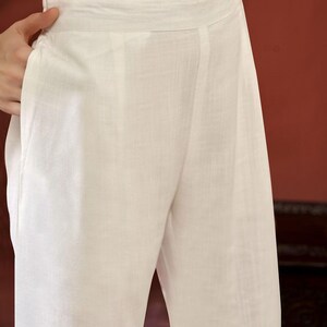 Puede incluir: Pantalones de lino blancos con una cintura ancha y un corte relajado. Los pantalones tienen un bolsillo visible y un dise&ntilde;o sencillo y elegante. La tela parece ligera y transpirable, adecuada para climas c&aacute;lidos.