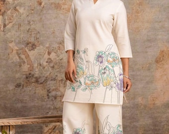 May include: Cream-colored two-piece outfit featuring a tunic top and wide-leg pants. The outfit is adorned with a floral design in shades of green, purple, and orange. The top has a v-neck and three-quarter sleeves. The pants have a matching floral pattern.