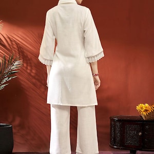 Puede incluir: Conjunto de dos piezas color crema. Presenta una t&uacute;nica con cuello y mangas tres cuartos con ribete de encaje en las mangas. Los pantalones a juego tambi&eacute;n tienen ribete de encaje en el dobladillo. El conjunto es de tejido ligero.