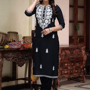 Può includere: Completo kurta ricamato nero. L'outfit nero presenta intricati ricami floreali bianchi sul corpetto, sulle maniche e sull'orlo. L'ensemble comprende un top lungo in stile tunica e pantaloni abbinati. Adatto per occasioni formali o festive.