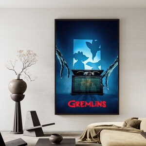 Puede incluir: Un p&oacute;ster enmarcado con el t&iacute;tulo de la pel&iacute;cula "Gremlins" en rojo. La obra representa una caja misteriosa con ojos brillantes, figuras sombr&iacute;as y manos inquietantes. El fondo es un degradado de azul.
