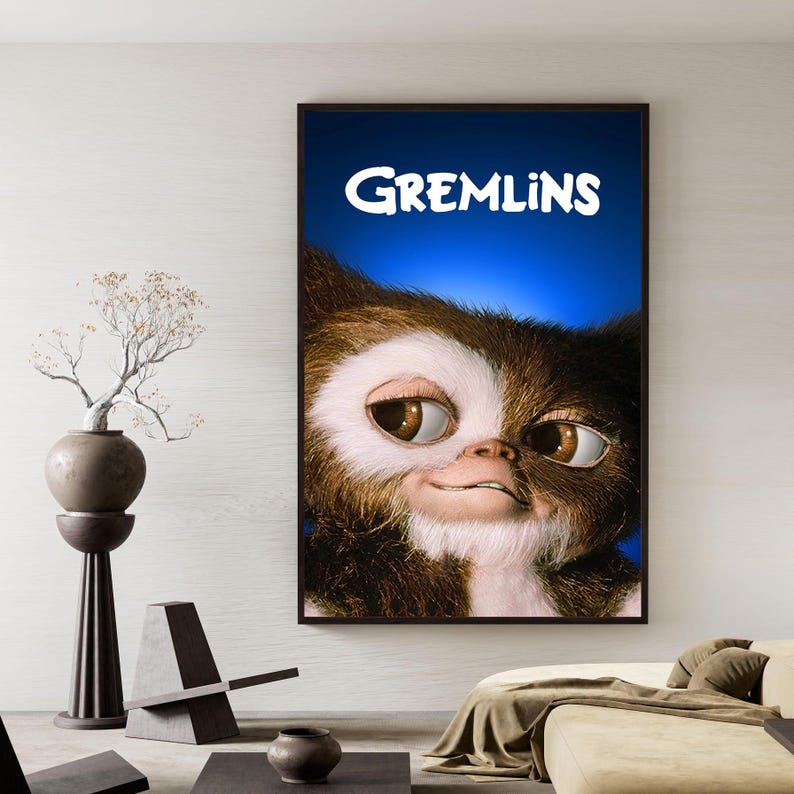 Puede incluir: Un p&oacute;ster enmarcado de la pel&iacute;cula Gremlins. El p&oacute;ster tiene un fondo azul con la palabra "Gremlins" en blanco. La imagen muestra un primer plano de la cara de un Gremlin, con pelaje marr&oacute;n y blanco y ojos grandes marrones.