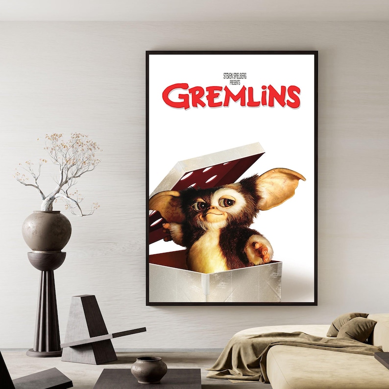 Puede incluir: Un p&oacute;ster enmarcado con el t&iacute;tulo de la pel&iacute;cula "Gremlins" en letras rojas. El p&oacute;ster muestra un personaje Gremlin saliendo de una caja. El Gremlin tiene pelaje marr&oacute;n y canela, orejas grandes y una expresi&oacute;n traviesa.