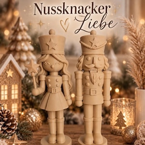 Può includere: Due statuette schiaccianoci color beige chiaro affiancate. La figura a sinistra ha capelli lunghi, una gonna e tiene una bacchetta a stella. La figura a destra ha baffi e barba. Sopra di loro, il testo recita Nussknacker Liebe con un cuore.