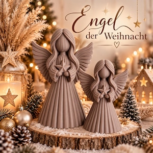 Puede incluir: Dos figuras de ángeles de color topo con texturas acanaladas, cada una sosteniendo una pequeña estrella. El texto "Engel der Weihnacht" aparece sobre las figuras. Los ángeles están colocados sobre una rodaja de madera circular.