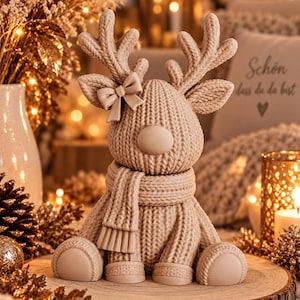 May include: A beige reindeer figurine with a textured knit pattern, featuring a smooth round nose, a small bow on one antler, and a matching scarf wrapped around its neck. The reindeer is in a seated position with its front and back legs visible.