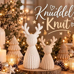 Könnte beinhalten: Zwei Rentierfiguren in Weiß und Beige mit einer gestrickten Oberflächenstruktur. Der Text "Knuddel Knut" steht in weißer Schreibschrift über den Figuren, ergänzt durch kleine Herz- und Sternsymbole in einer festlichen Umgebung.