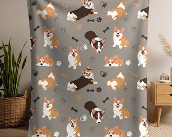 Könnte beinhalten: Eine graue Decke mit einem sich wiederholenden Muster von Cartoon-Corgi-Hunden in verschiedenen Posen. Die Hunde sind in Braun-, Weiß- und Schwarztönen gehalten. Das Design umfasst auch Pfotenabdrücke, Herzen und Knochen.
