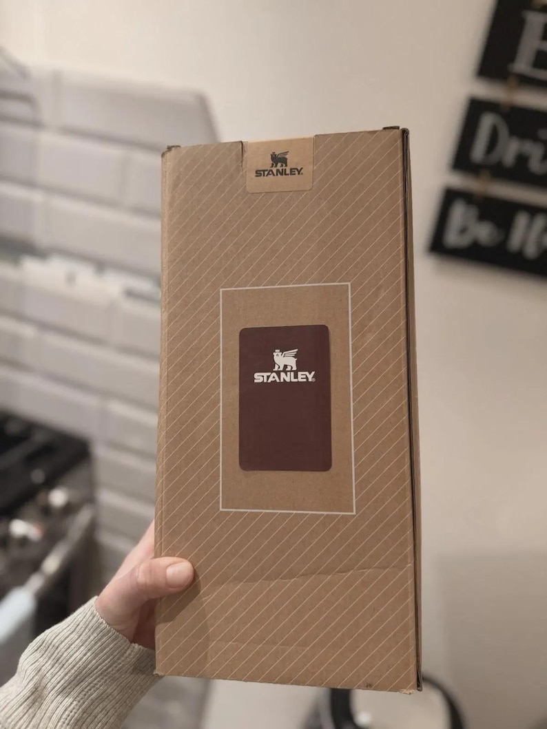 Puede incluir: Caja de cart&oacute;n marr&oacute;n de la marca Stanley, con l&iacute;neas diagonales. Tiene una etiqueta rectangular marr&oacute;n con el logotipo de Stanley. El logotipo de Stanley tambi&eacute;n est&aacute; impreso en la parte superior de la caja.