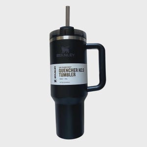 May include: Black Stanley Quencher H2.0 Tumbler with a handle and a straw. The tumbler has a black lid and a white label with the text "QUENCHER H2.0 TUMBLER" and the Stanley logo. It holds 40 oz (1.18 L).