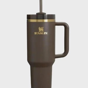Puede incluir: Un vaso Stanley marr&oacute;n con asa y pajita. El vaso tiene una banda dorada y el logotipo de Stanley en dorado. Est&aacute; dise&ntilde;ado para mantener las bebidas calientes o fr&iacute;as durante horas. Capacidad aproximada de 1,2 litros.
