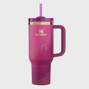 May include: A pink Stanley tumbler with a handle and straw. The tumbler has a gold rim and the Stanley logo. It features a pattern of gold stars and the word "Barbie" on the side.