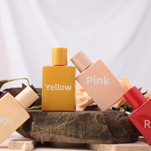 May include: Four rectangular perfume bottles in yellow, pink, beige, and red, each with a matching cap. The bottles are arranged on a stone surface with floral and wooden accents, and the names of the colors are printed on the bottles.