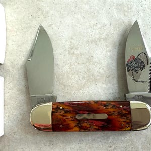 May include: A pocket knife with a red and brown handle and two blades. One blade has a turkey design and the text "Gobbler" and "Texas Pride".