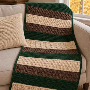 Può includere: Una coperta rettangolare all'uncinetto con strisce orizzontali in verde scuro, marrone e crema. Il design incorpora motivi strutturati alternati, tra cui punti a treccia, punti a nocciolina e punti a muschio su tutta la superficie.