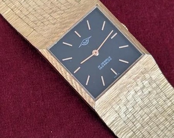 May include: A gold-tone wristwatch with a textured, woven-style metal strap and a square black dial. The dial features gold-tone hour markers, thin gold-tone hands, and the text "TRUS", "17 JEWELS", "INCA-BLOC", and "SWISS" printed in white.