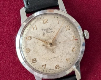 May include: A vintage Rotary wristwatch with a silver-tone round case and a black leather strap. The off-white dial features gold-tone Arabic numerals, gold-tone hands, and the text Rotary, 17 Jewels, Incabloc, and Swiss Made printed on the face.