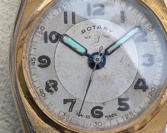 May include: A vintage Rotary wristwatch with a round, off-white dial featuring black Arabic numerals, a gold-tone bezel, and a dark brown leather strap. The watch face displays the text Rotary and Swiss Made, with luminous hour and minute hands.