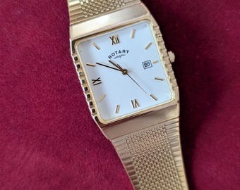 May include: A gold-tone wristwatch with a rectangular case and a matching mesh metal strap. The white dial features black Roman numeral markers at the twelve, six, and nine o'clock positions, thin black hands, and a date window displaying the number 20.