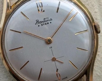 May include: A vintage Bentima Star wristwatch with a gold-tone case, a silver dial, and a dark brown leather strap. The dial features gold-tone hour markers, a numeral 12, thin gold hands, a sub-dial for seconds, and the text Bentima Star 17 Swiss Made.