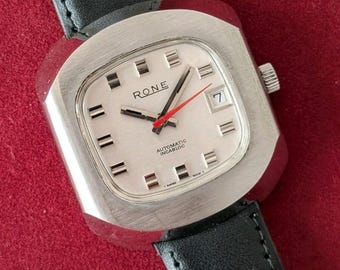 May include: A Rone automatic wristwatch with a silver-toned square case, a white dial featuring silver hour markers, a red second hand, and a date window at the three o'clock position. The watch is attached to a black leather strap with stitching.