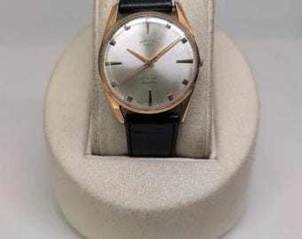 Könnte beinhalten: Eine Vintage-Armbanduhr von Rotary mit einem runden goldfarbenen Gehäuse, einem silbernen Zifferblatt mit Sonnenschliff, goldfarbenen Indizes und Zeigern sowie einem schwarzen Lederarmband. Das Zifferblatt zeigt das Rotary-Logo und 17 Jewels Incabloc.